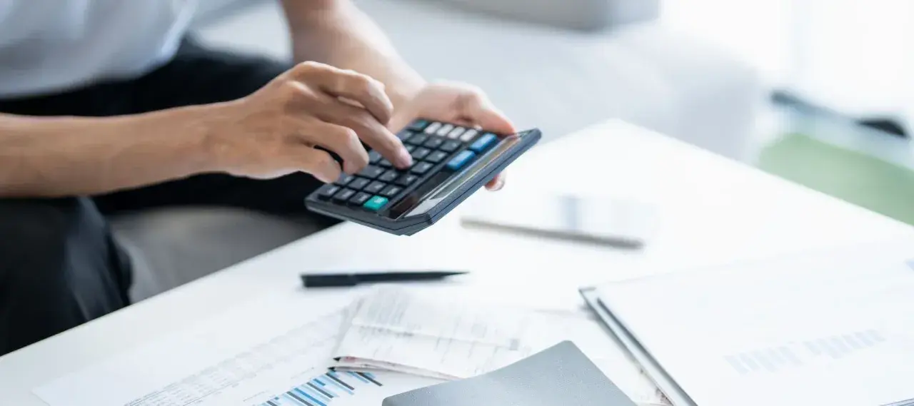 Persona calculando la declaración de la renta con calculadora y documentos.
