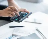 Persona calculando la declaración de la renta con calculadora y documentos.