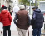 Tres personas mayores caminan por la calle, una con bastón, reflexionando sobre la **pensión mínima**.