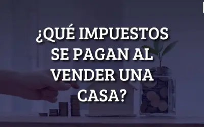 ¿Qué impuestos se pagan al vender una casa? Mano colocando monedas en una alcancía con una planta, junto a una casa de juguete y pilas de monedas.