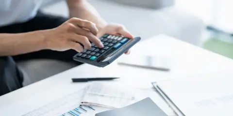 Persona calculando la declaración de la renta con calculadora y documentos.