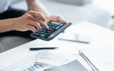 Persona calculando la declaración de la renta con calculadora y documentos.