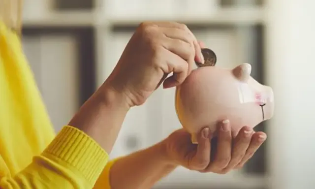 Manos introducen una moneda en una hucha rosa, simbolizando el ahorro para recuperar plan de pensiones nueva ley.