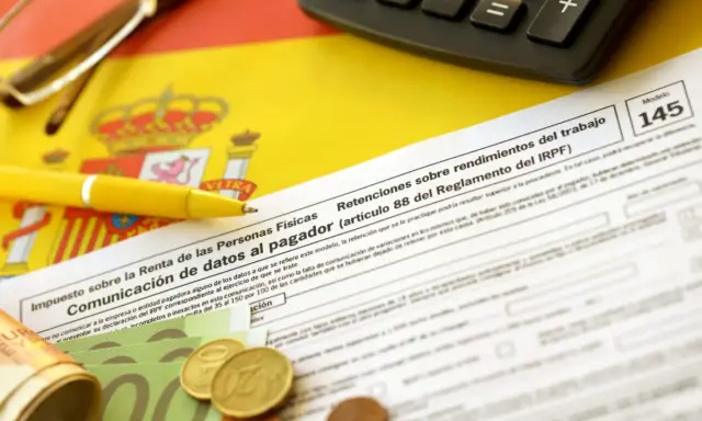 Documentos fiscales españoles, calculadora, bolígrafo amarillo y dinero, listos para cuando se pagan impuestos en España.