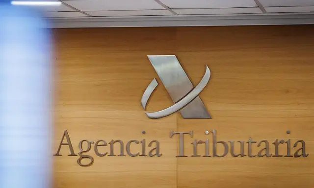 Logo y nombre de la Agencia Tributaria en una pared de madera.