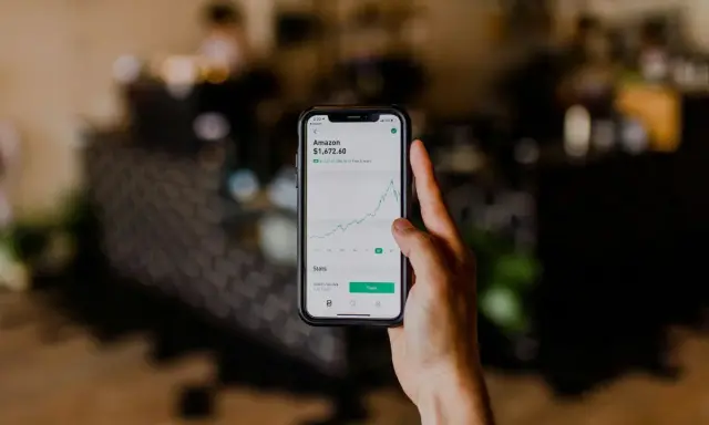 Mano sosteniendo un teléfono que muestra el gráfico de acciones de Amazon, una opción para saber donde invertir dinero.