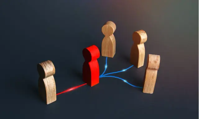 Figuras de madera conectadas por líneas de luz. Una figura roja central actúa como nodo, conectando a otras figuras, representando el papel de intermediarios financieros.