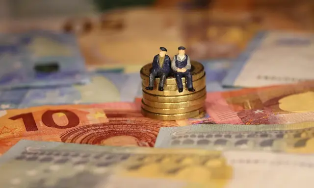 Dos figuritas sentadas en monedas de oro sobre billetes de euros. Reflexionan: como puedo cotizar los años que me faltan.