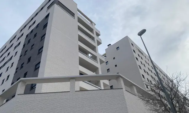 Modernas viviendas VPO en Alicante, edificios de ladrillo blanco y gris con balcones, bajo un cielo nublado.