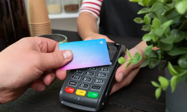Pago sin contacto con una tarjeta prepago. Una mano acerca una tarjeta de colores a un terminal de pago.
