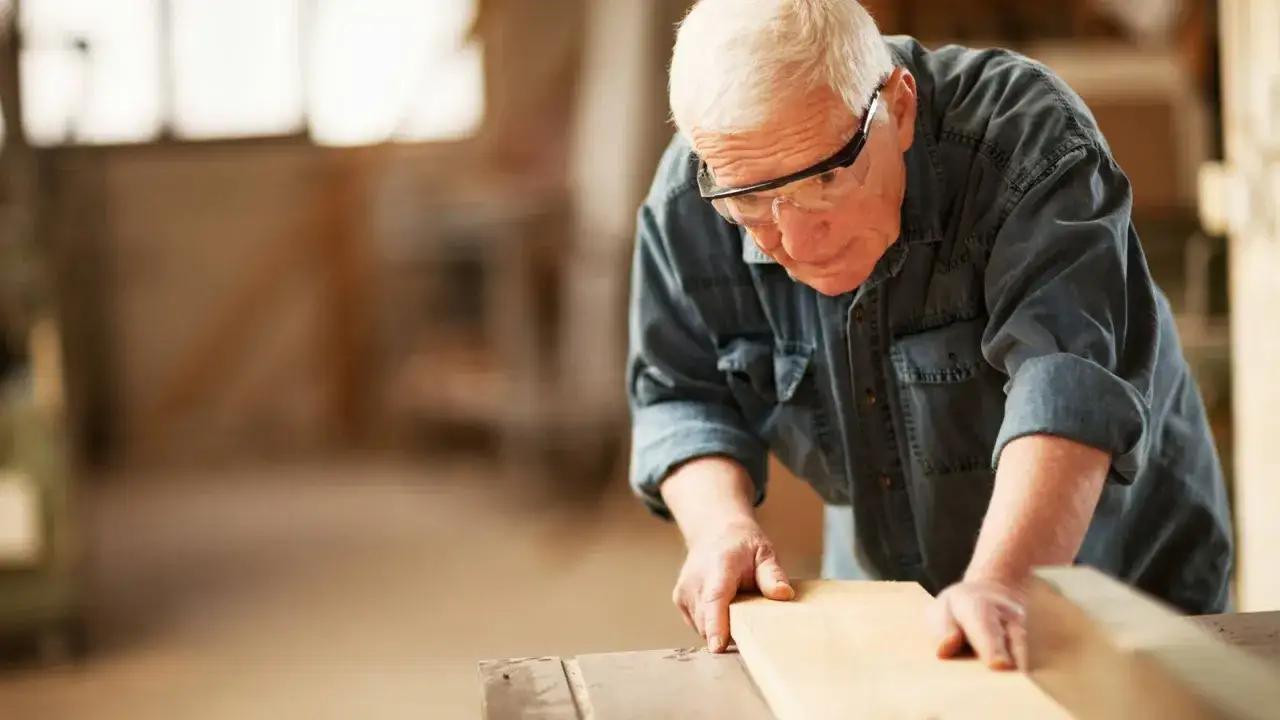 Hombre mayor con gafas de seguridad trabajando la madera, ejemplo de jubilaci&oacute;n activa.