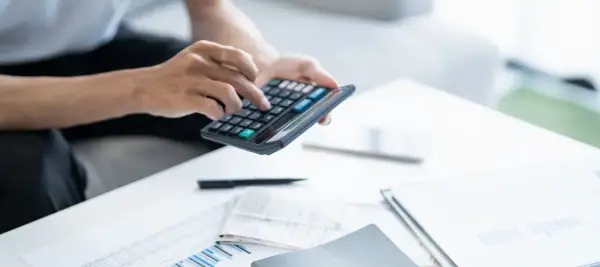 Persona calculando la declaración de la renta con calculadora y documentos.