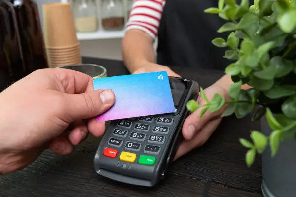 Pago sin contacto con una tarjeta prepago. Una mano acerca una tarjeta de colores a un terminal de pago.